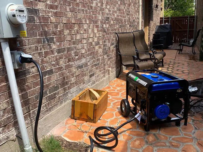 A generator is plugged into an outlet on the side of a brick building.