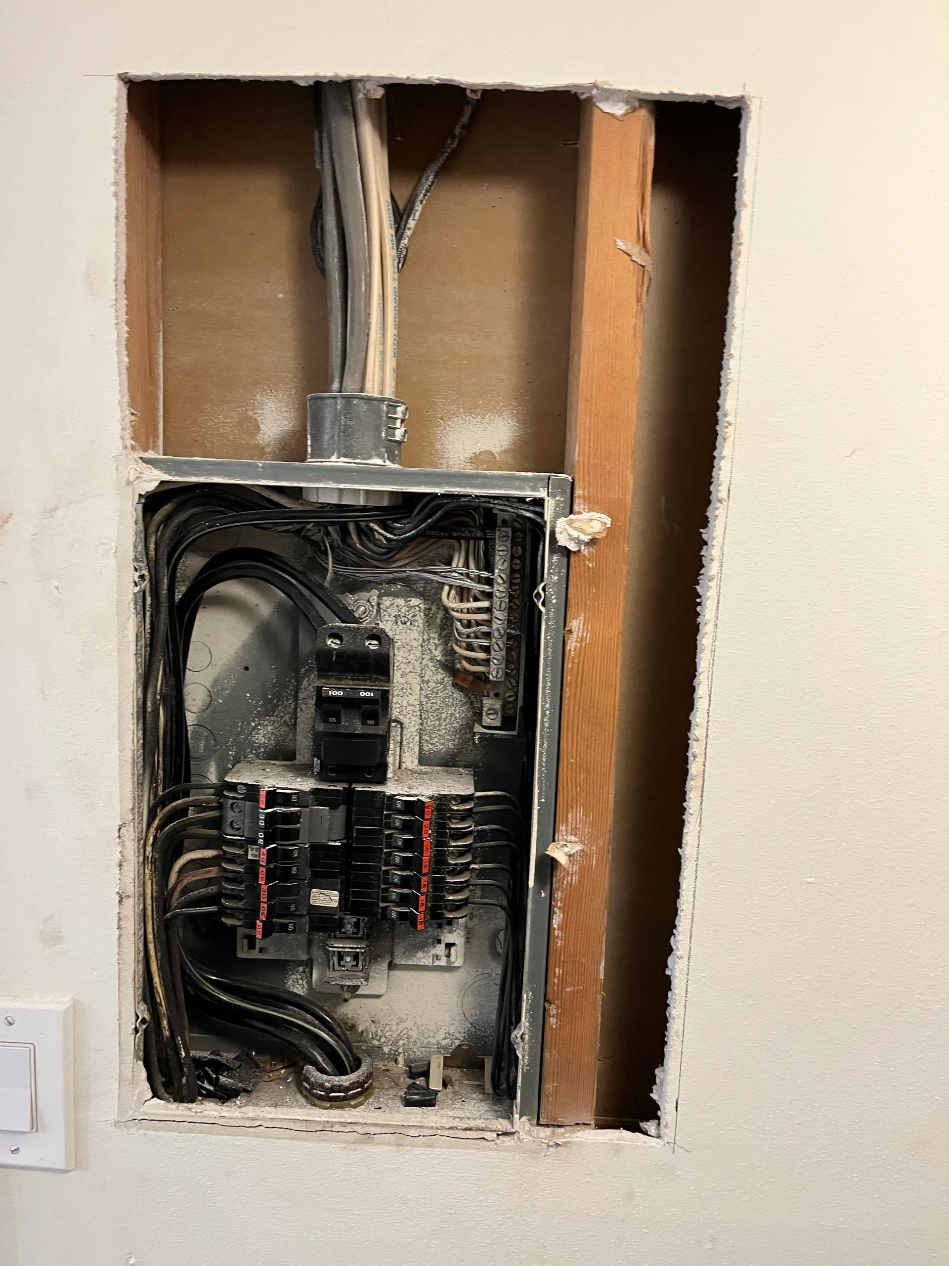 An electrical box is sitting in a hole in a wall.