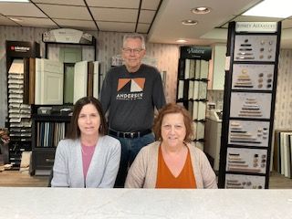 Three people standing in a kitchen showroom. Two women seated, one man standing behind them. They are smiling. Three people standing in a kitchen showroom. Two women seated, one man standing behind them. They are smiling.