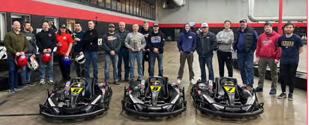 A group of people standing behind three go-karts in an indoor facility.