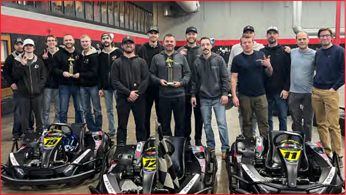 A group of people stands in an indoor go-karting facility with three go-karts in the foreground.