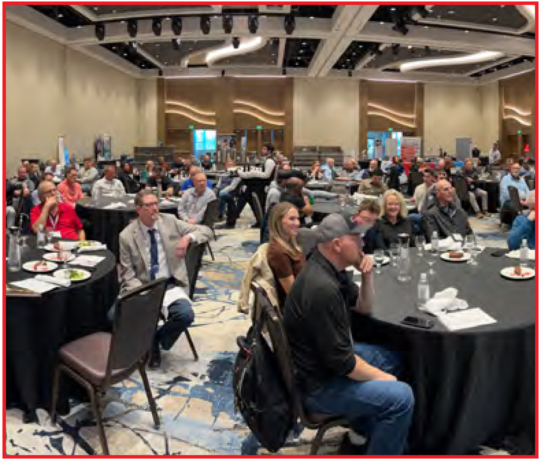 Conference audience seated at round tables in a large hotel ballroom during a presentation