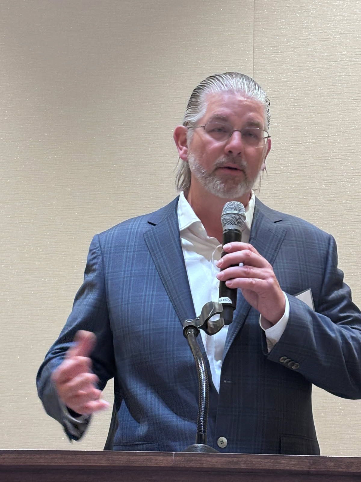 Man in a blue suit speaks into a microphone at a podium, gesturing with his hands.