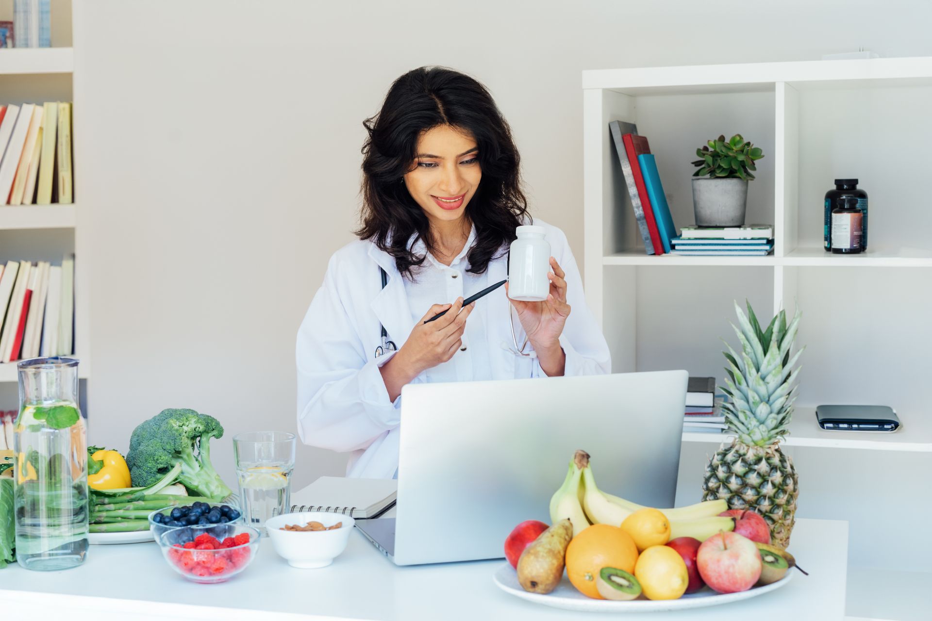 A female doctor is sitting at a desk with a laptop and a cup of coffee.