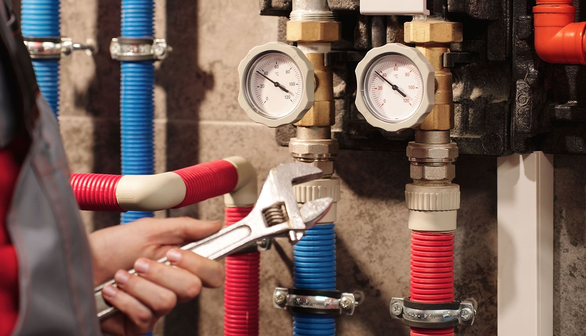 A technician using a wrench to adjust a system of pipes and pressure gauges in a utility room.