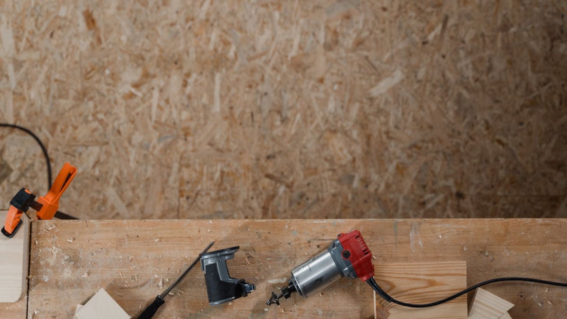 Escena de carpintería: taladro eléctrico sobre una superficie de madera con abrazaderas y herramientas cerca.