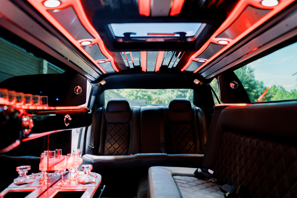 Interior of a limousine with red lighting and leather seating. Drinks on a bar are visible.