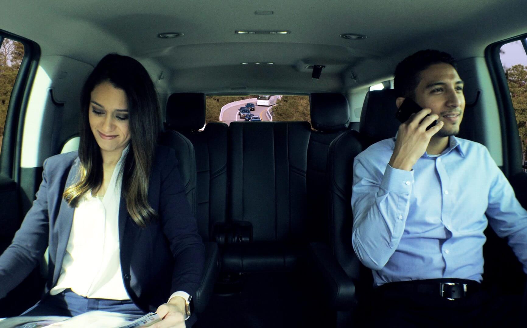 Woman looks at document, man on phone, both in a car.