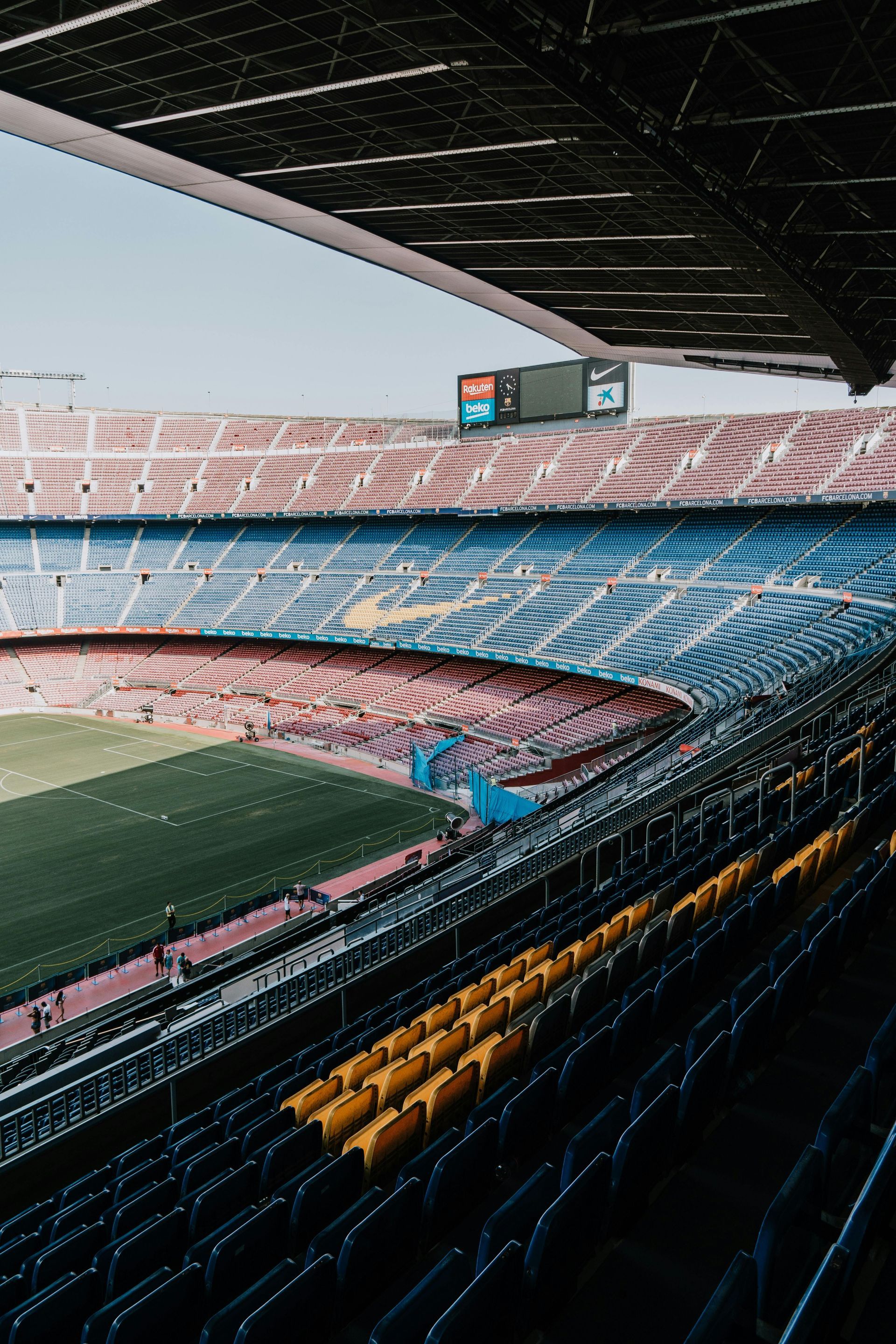 Empty stadium with rows of seats in yellow, red, and blue. Green field visible.