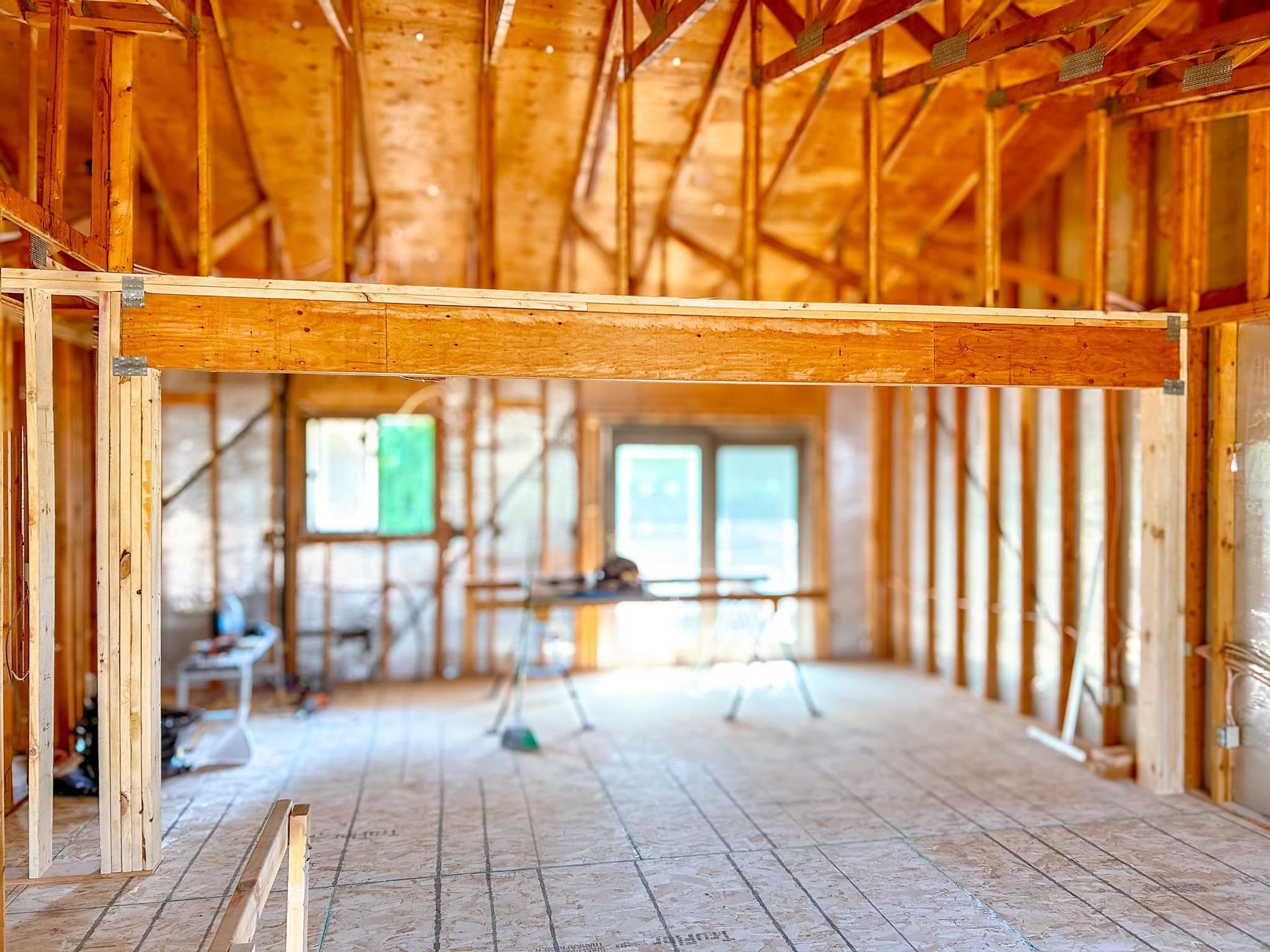 Interior of a building under construction, wooden framework, open space, light wood, visible windows in the background.
