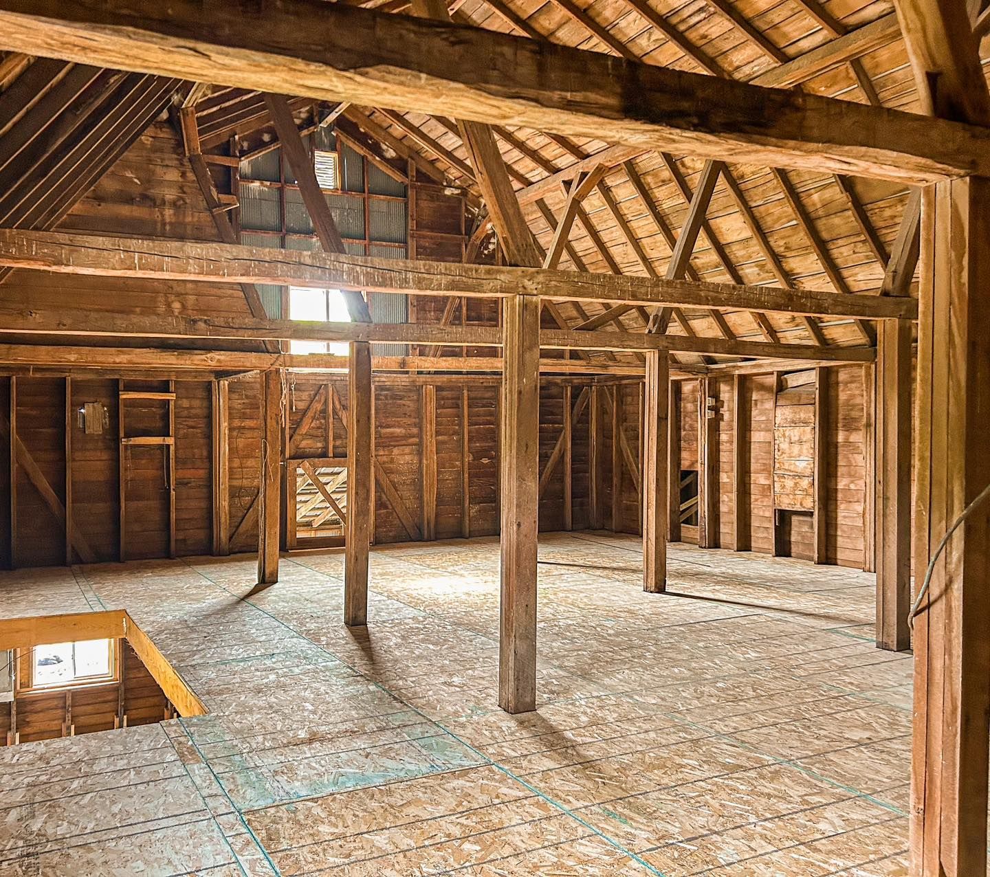 Interior of a rustic wooden barn with exposed beams and plywood floors and walls.