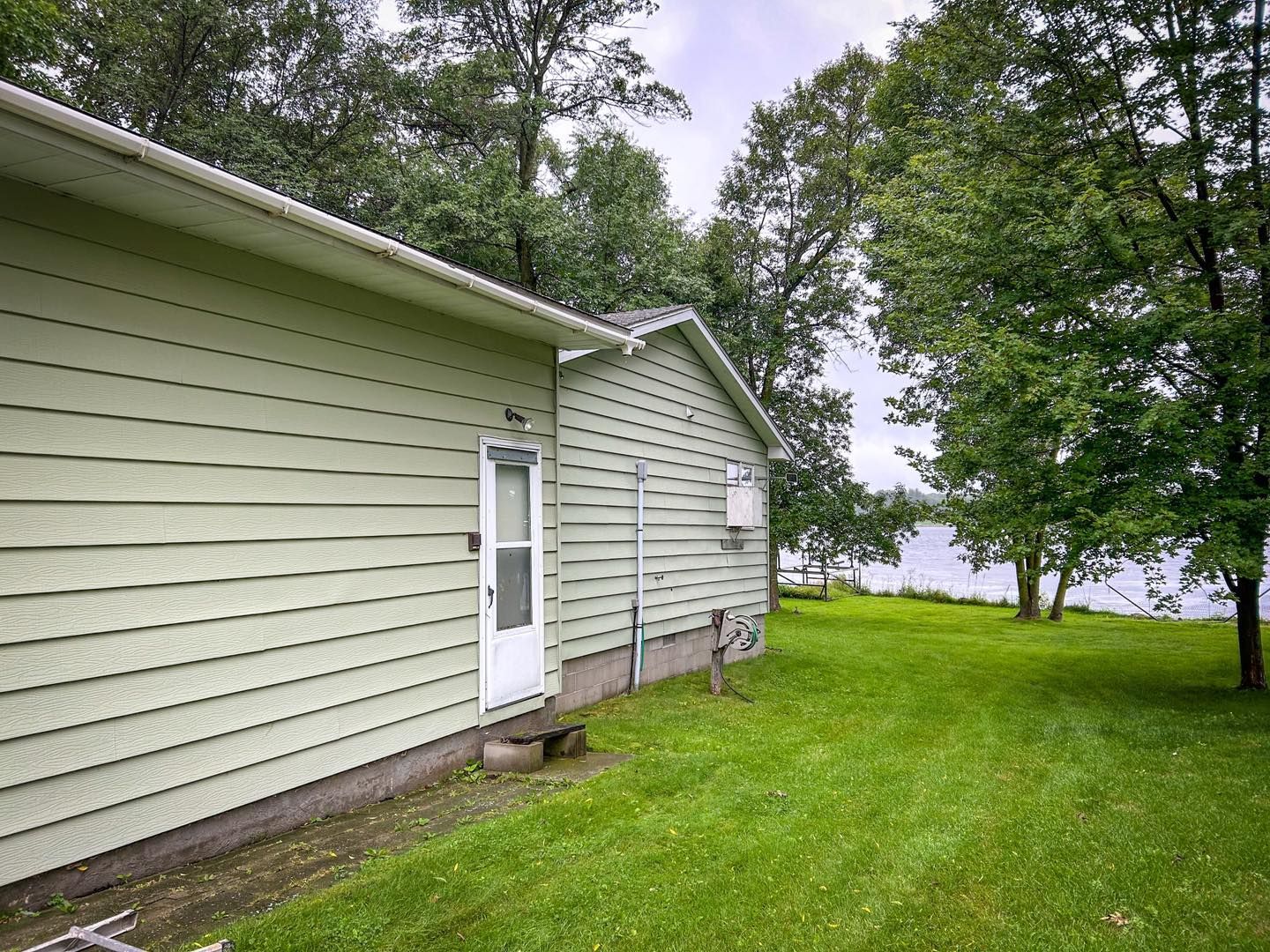 Light green house by a body of water, with trees and green grass.