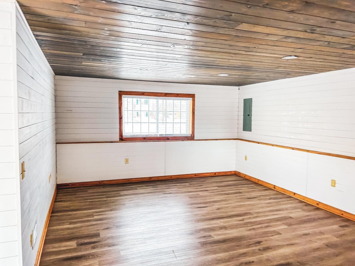 Empty room with wood floor, paneled white walls, window, and wood ceiling.