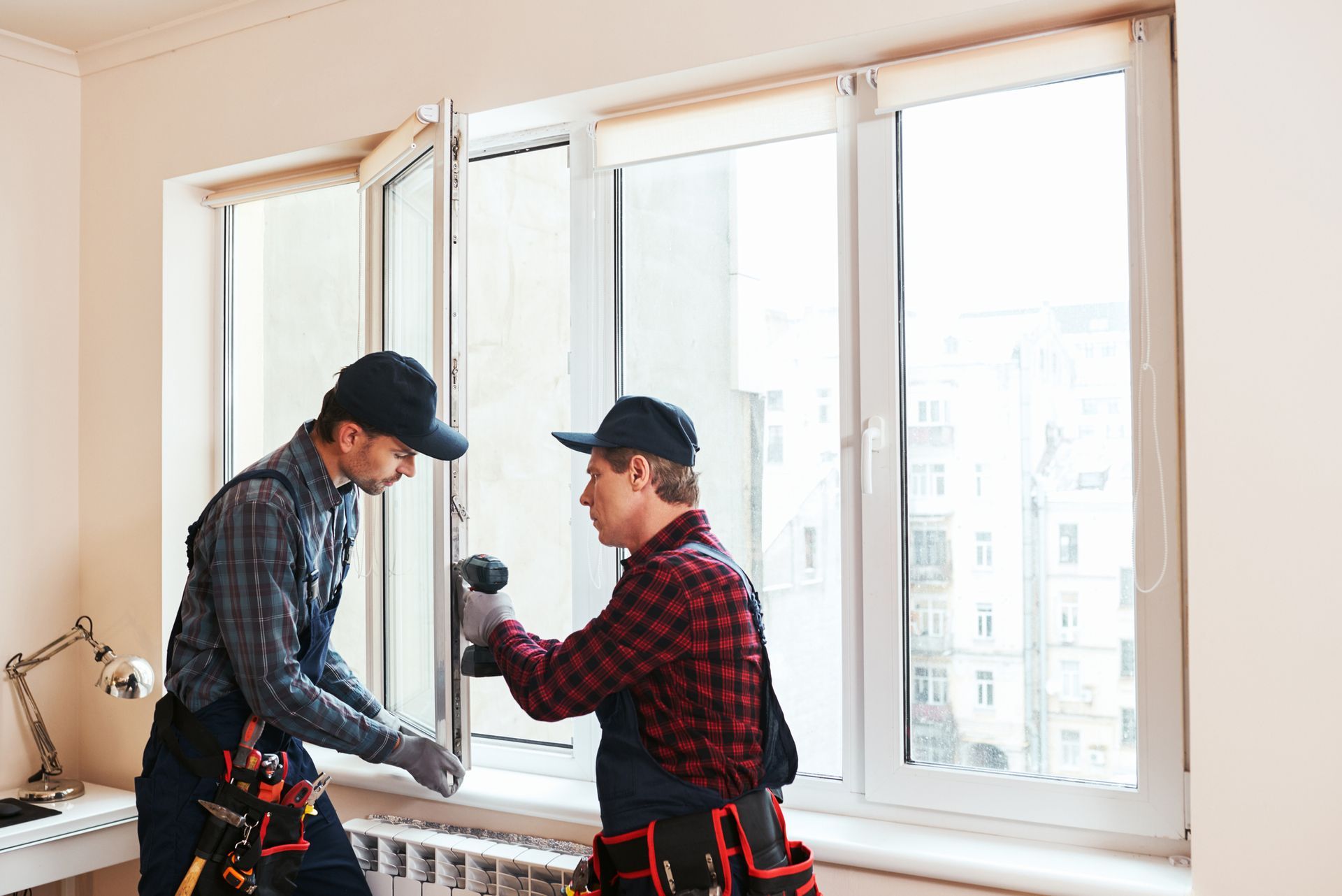 Two workers installing a white window. One uses a power drill.