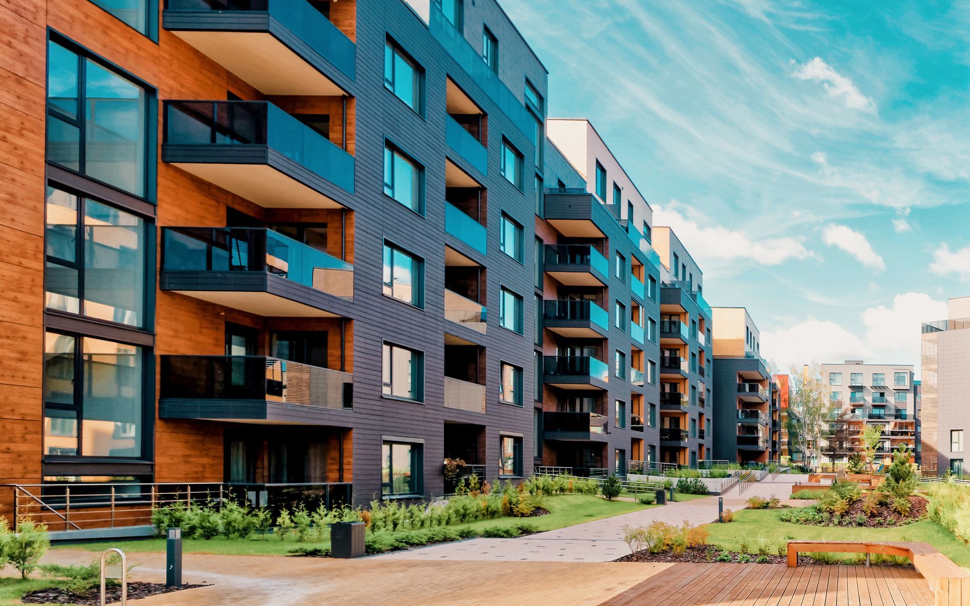 Modern apartment buildings with balconies, blue sky, and greenery.