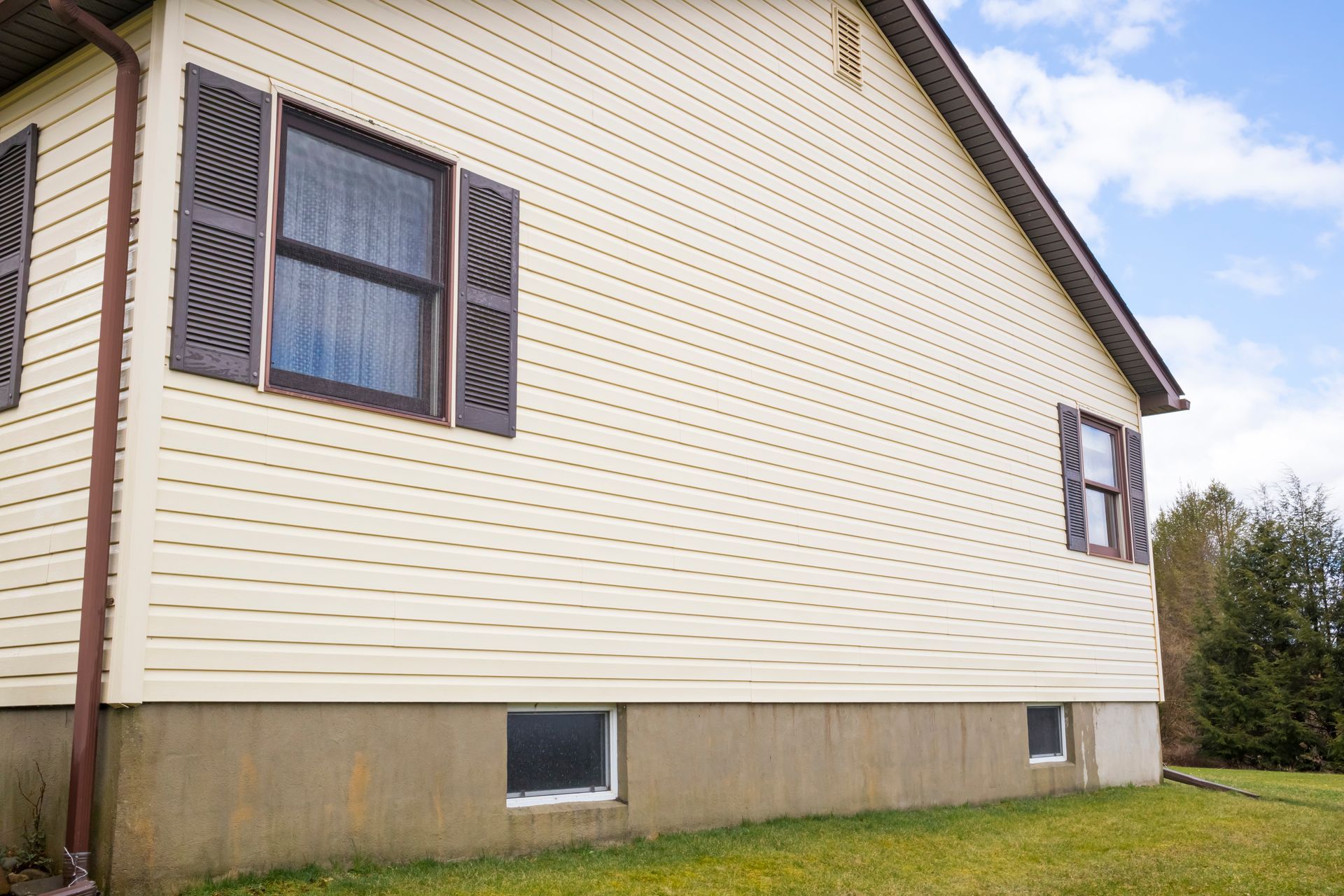 Beige house with brown shutters and a green lawn.