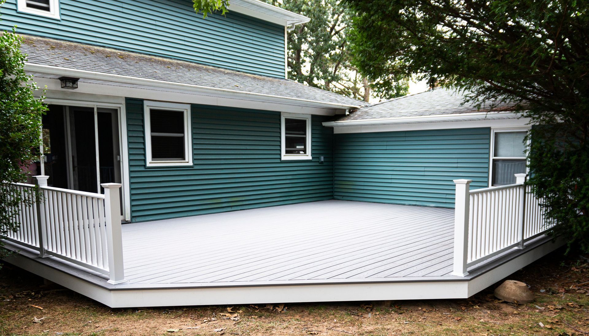 Teal house with white deck and railing, surrounded by greenery.