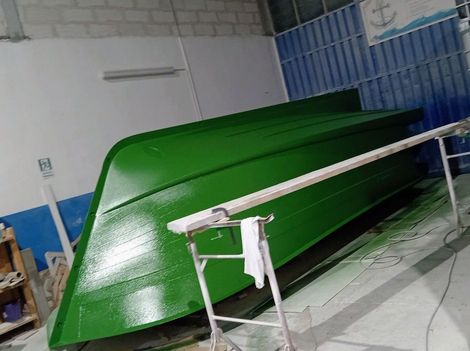 Lo scafo di una barca, appena verniciato di un verde brillante, poggia su un supporto metallico all'interno di un'officina.