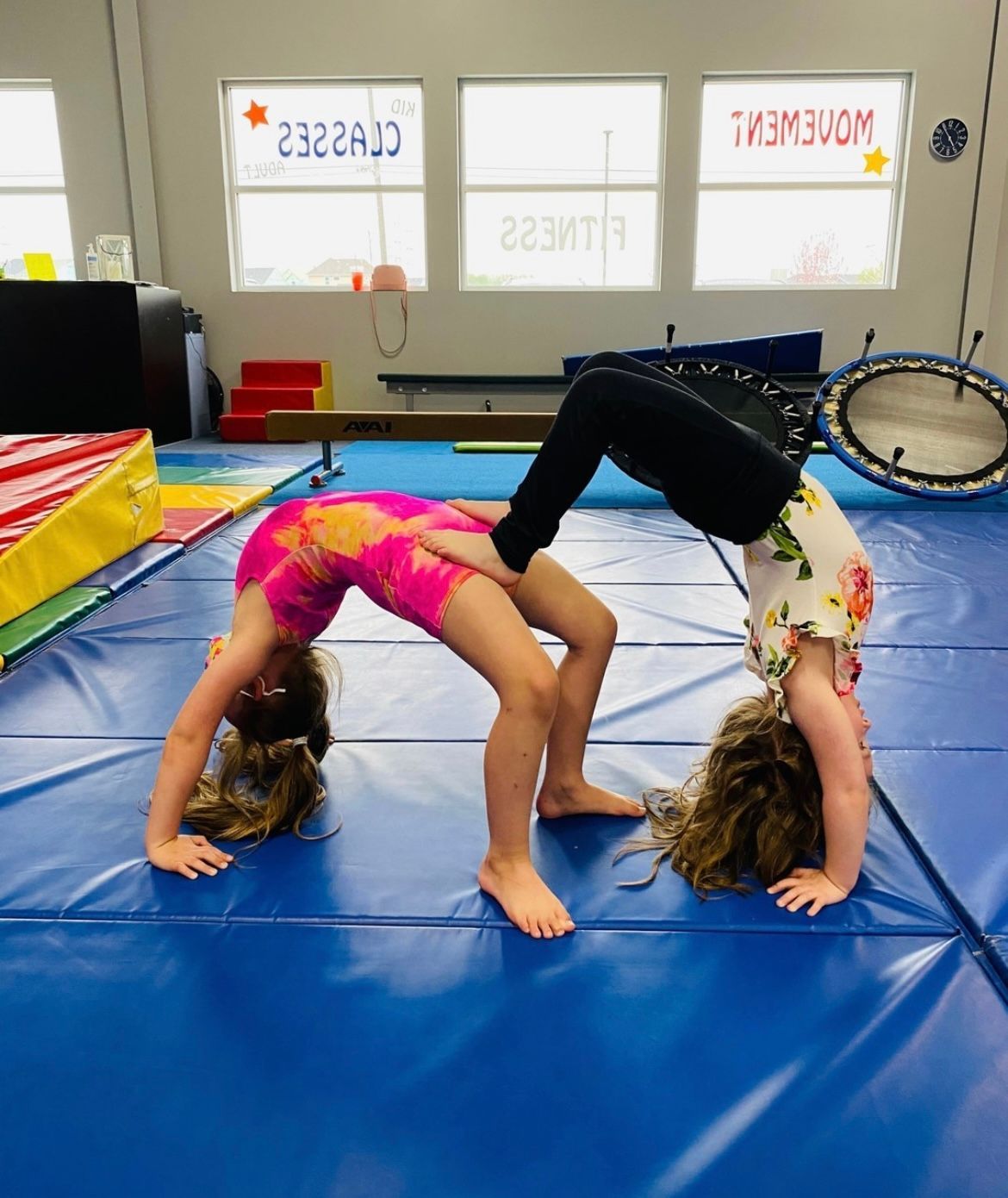 Two young girls are doing a handstand on a blue mat.