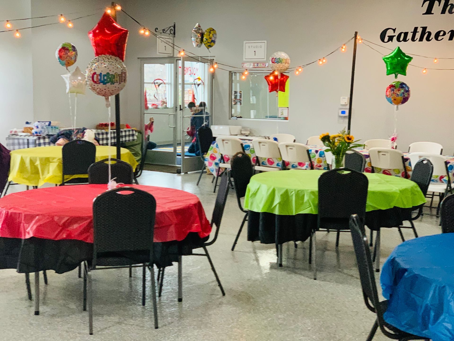 A room with tables and chairs decorated with balloons and a sign that says the gather