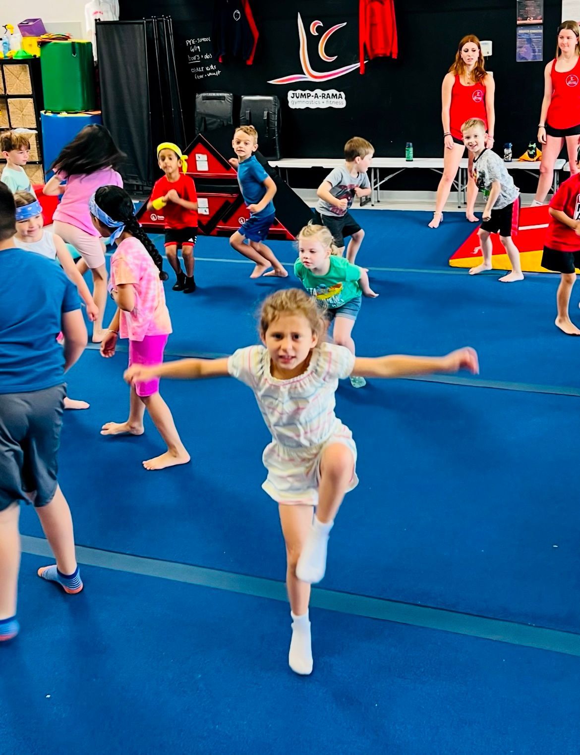 A group of children are doing exercises on a blue mat in a gym.