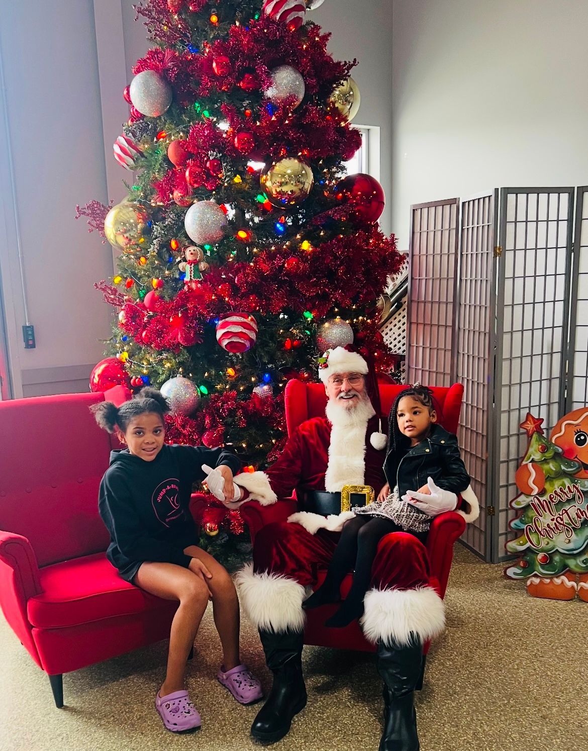 Two little girls are sitting next to santa claus in front of a christmas tree.