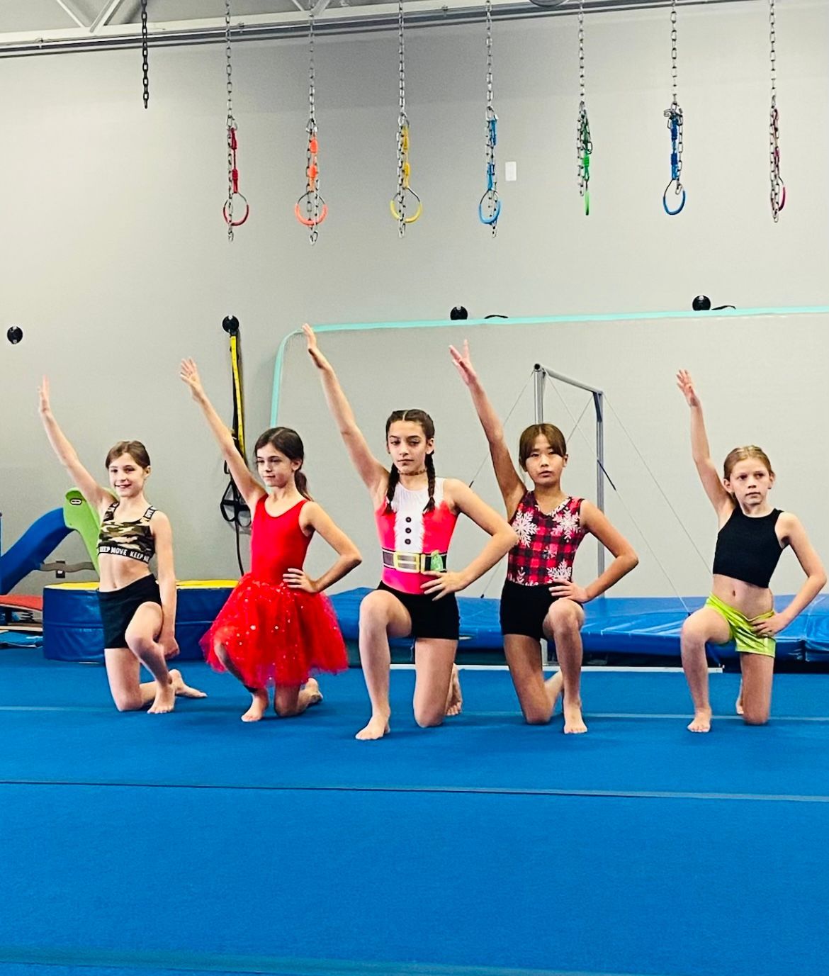 A group of young girls are kneeling on the floor with their arms in the air.