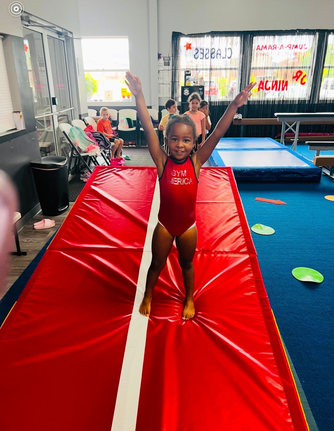 A little girl is standing on a red mat in a gym.