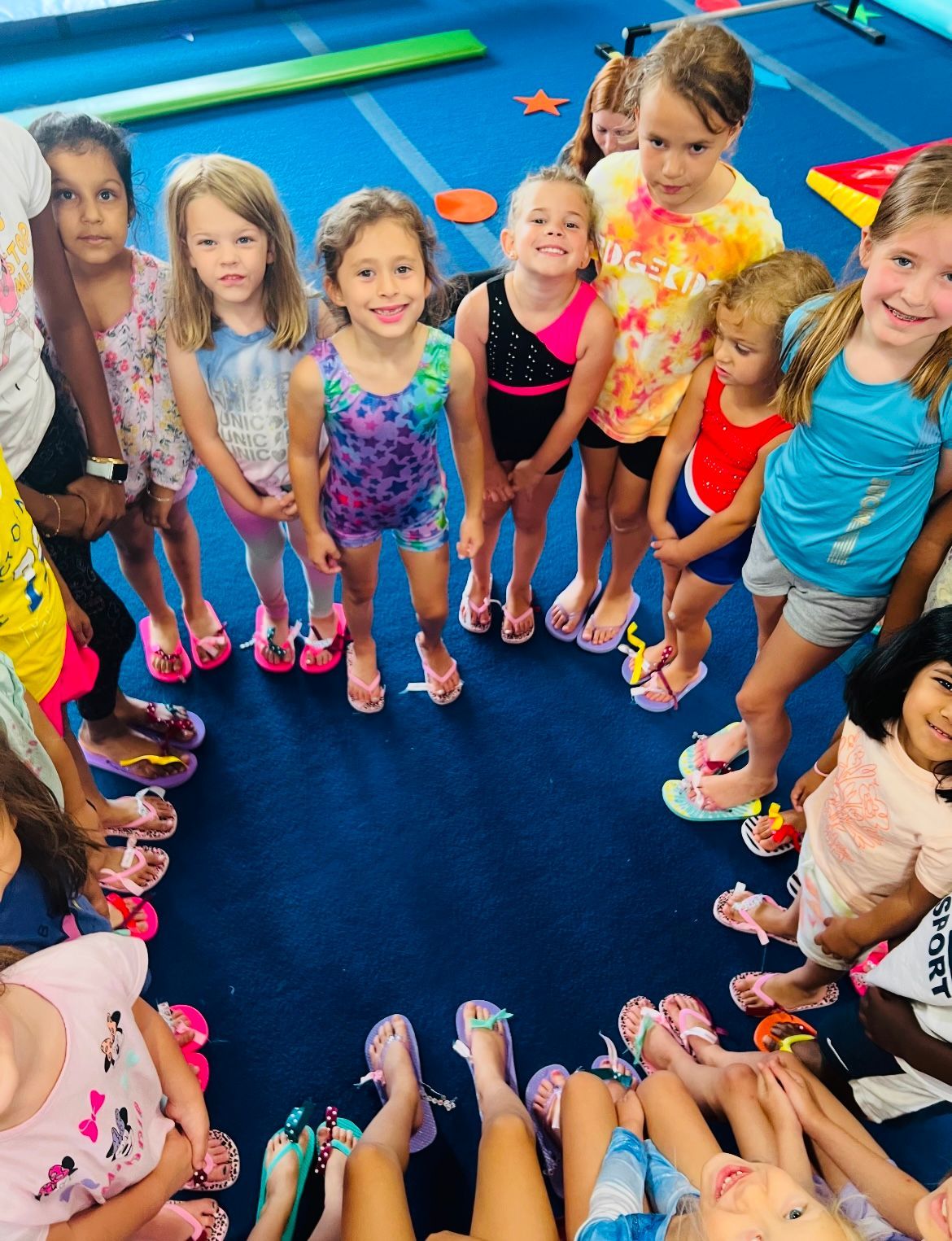 A group of young girls are standing in a circle with their feet on the floor.