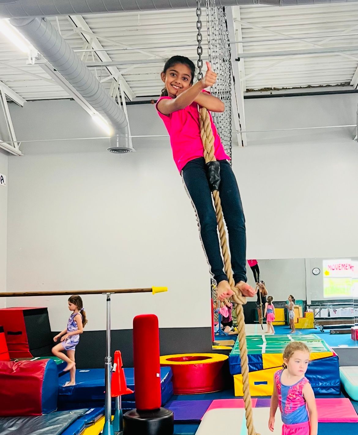 A young girl is climbing a rope in a gym.