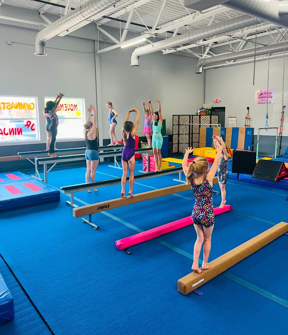 A group of young girls are standing on balance beam in a gym.