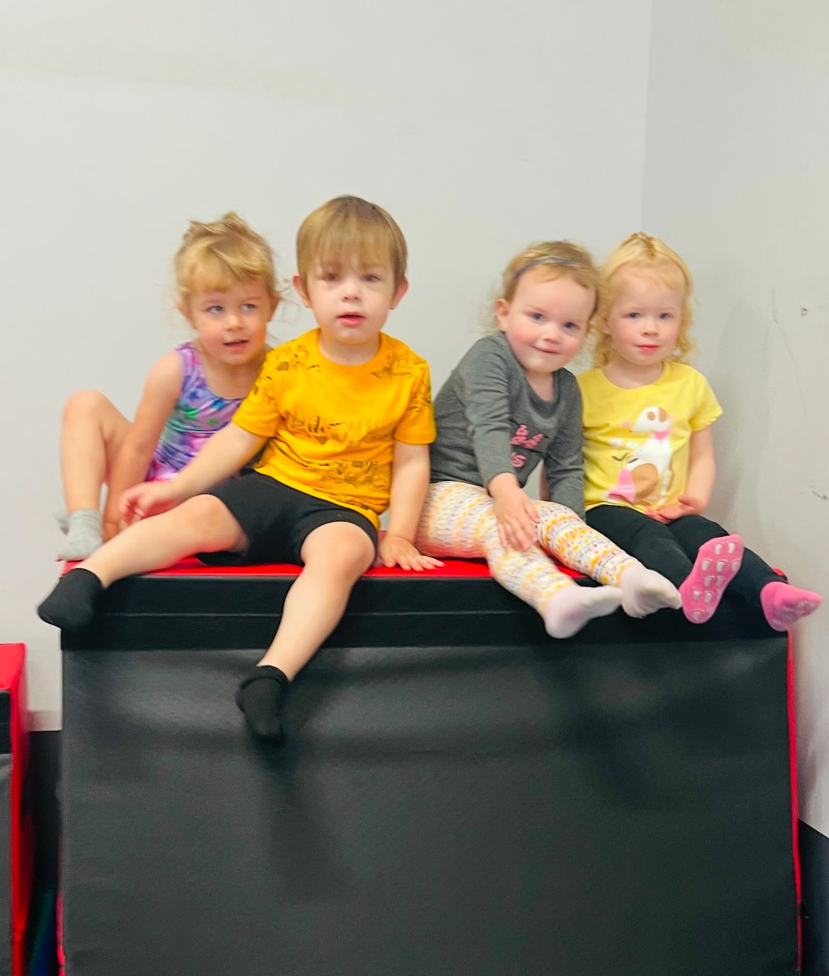 A group of young children are sitting on top of a black mat.