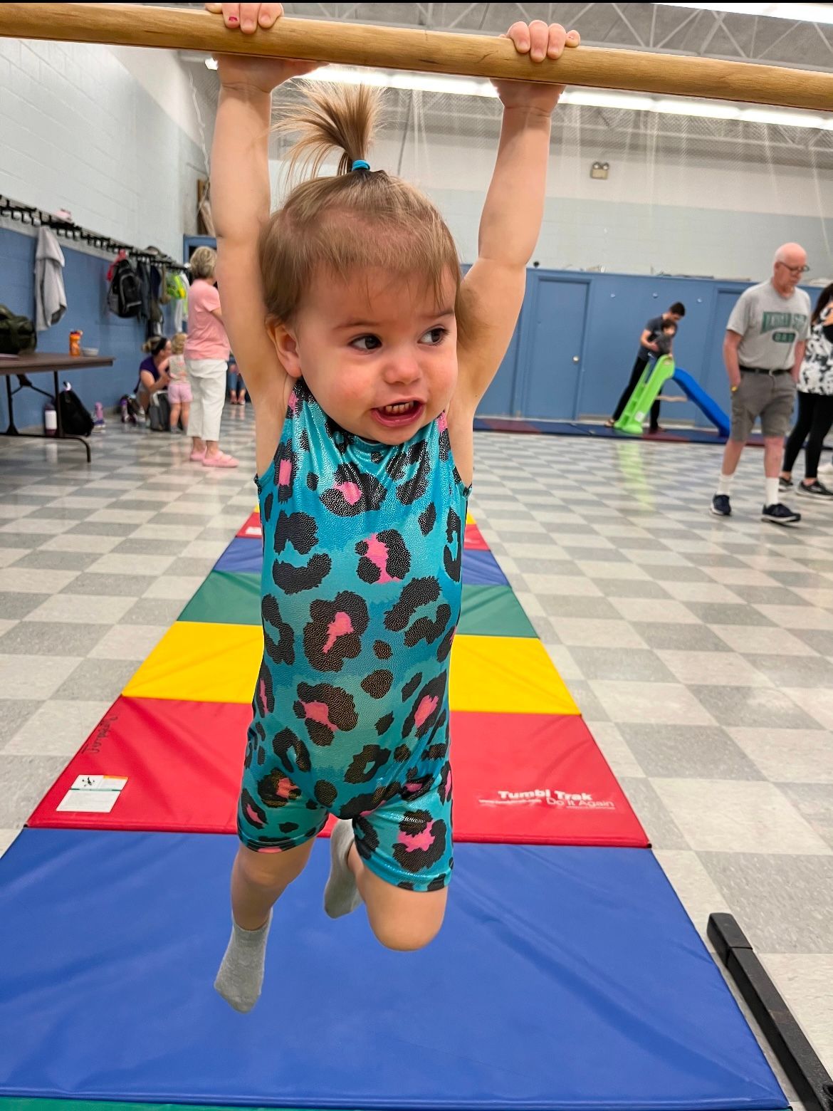 A little girl is hanging on a bar in a gym.