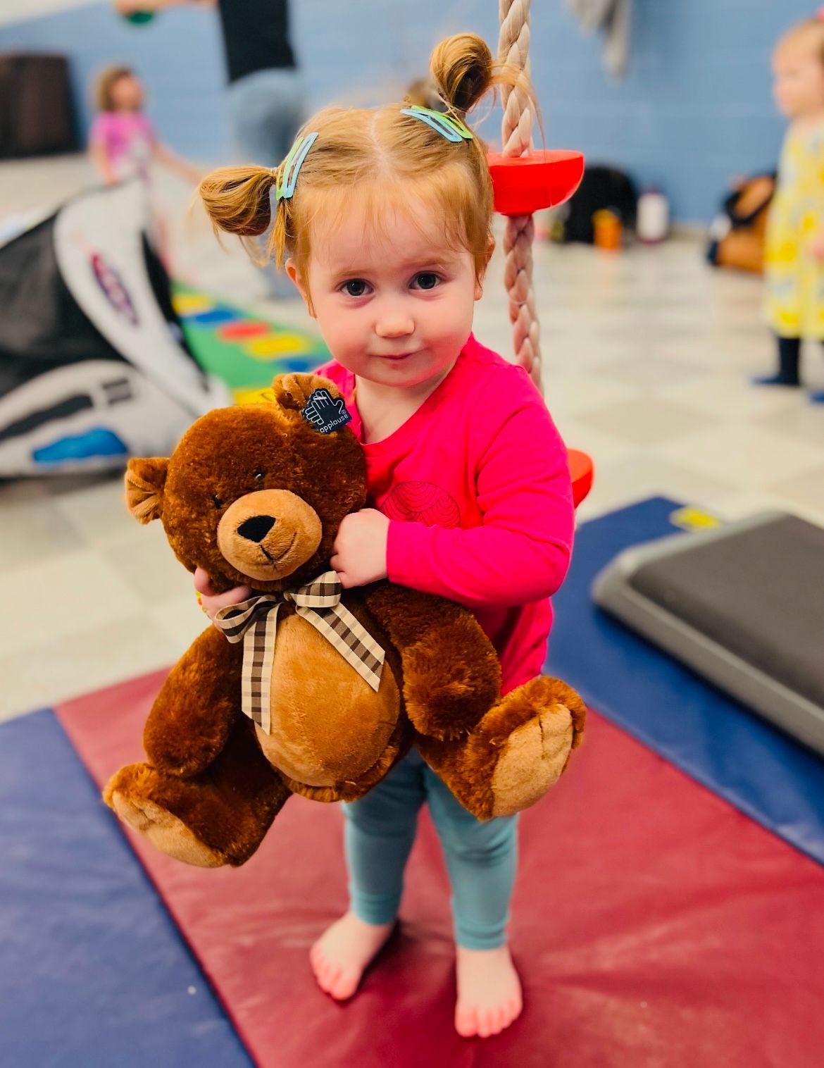 A little girl is holding a teddy bear on a swing.