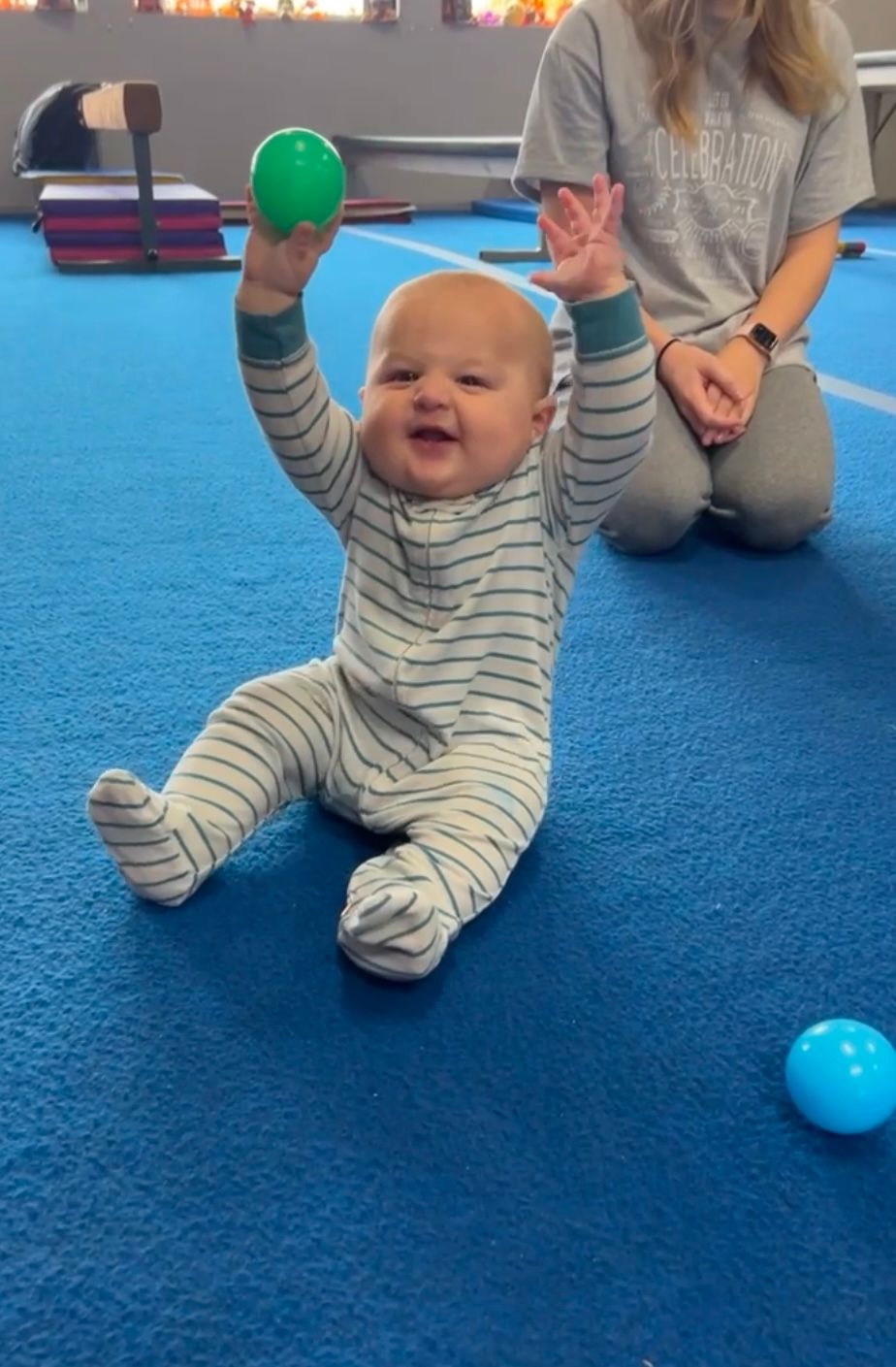 A baby is sitting on the floor holding a green ball