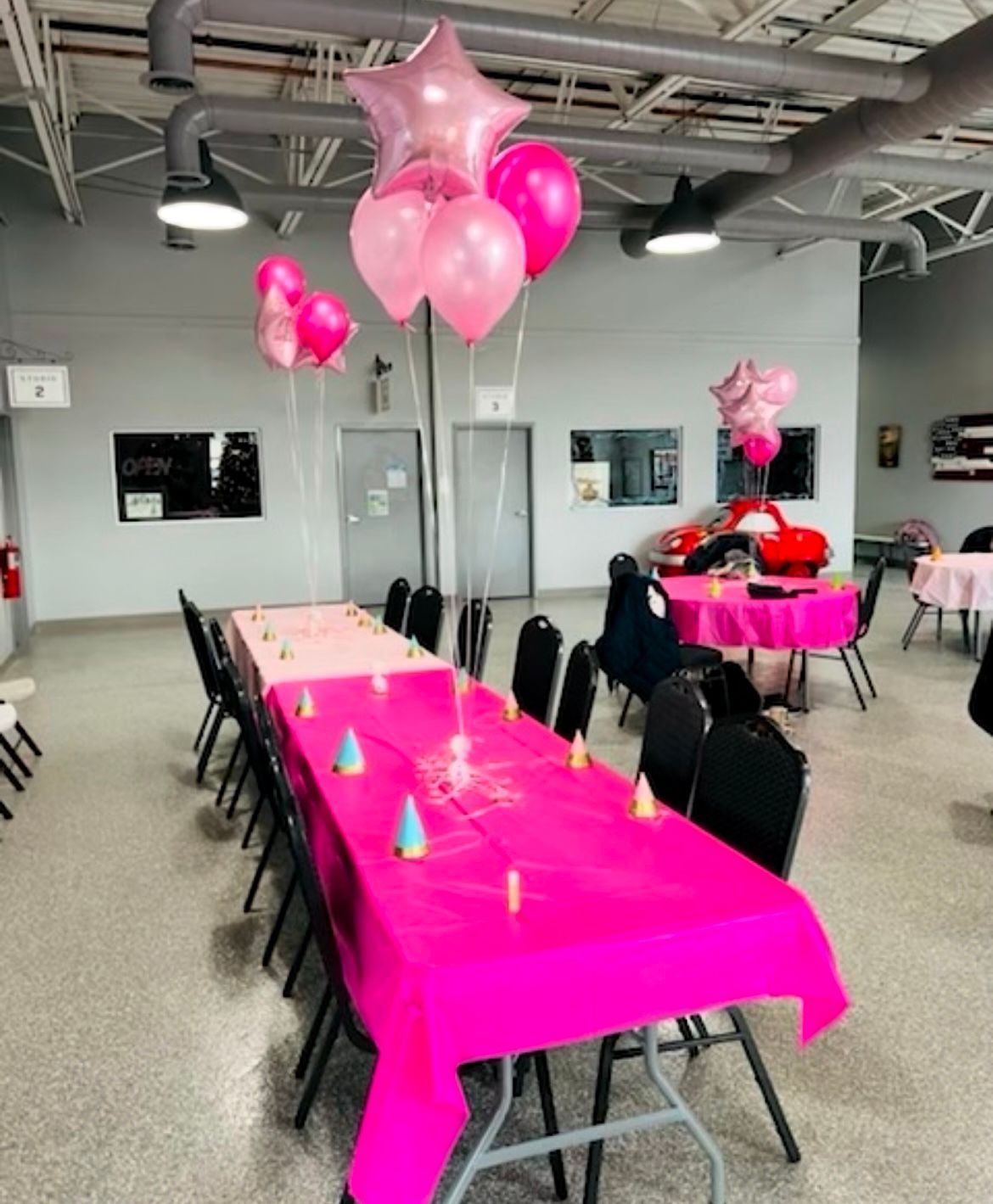 A room with pink tables and chairs and balloons hanging from the ceiling