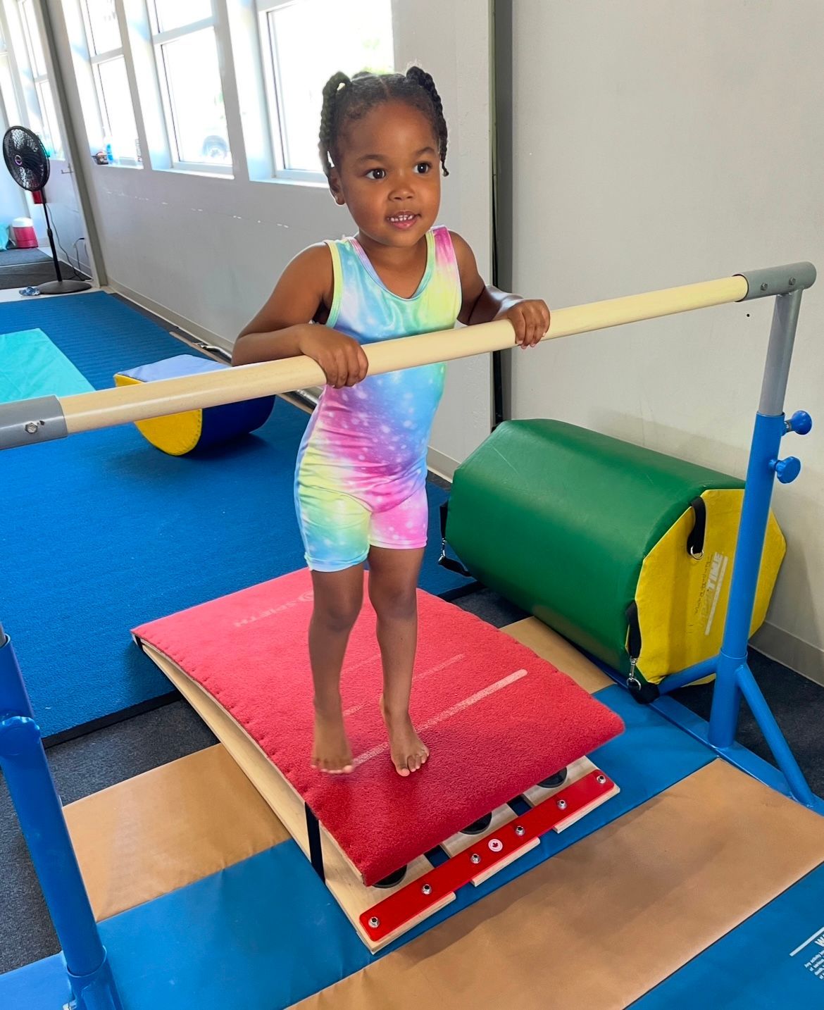 A little girl is standing on a balance beam in a gym.