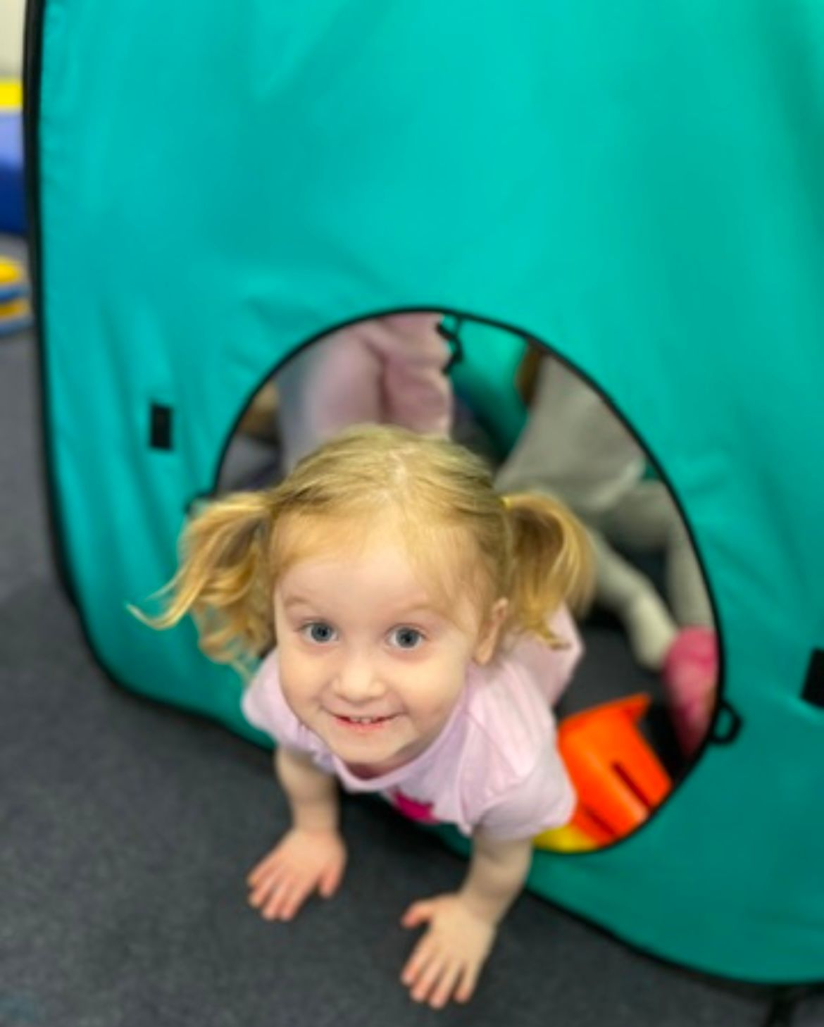 A little girl is crawling out of a teal tent.