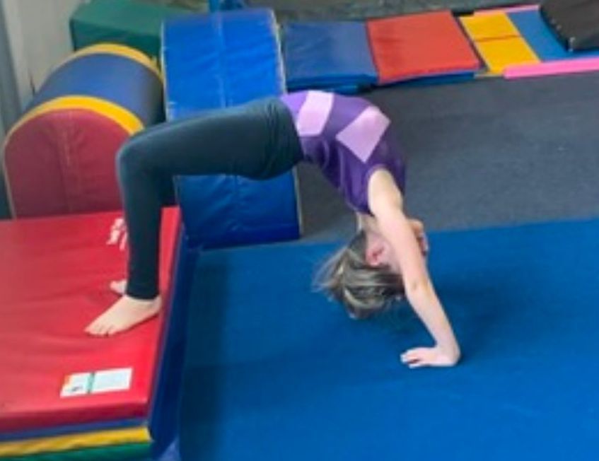 A young girl is doing a handstand on a blue mat in a gym.