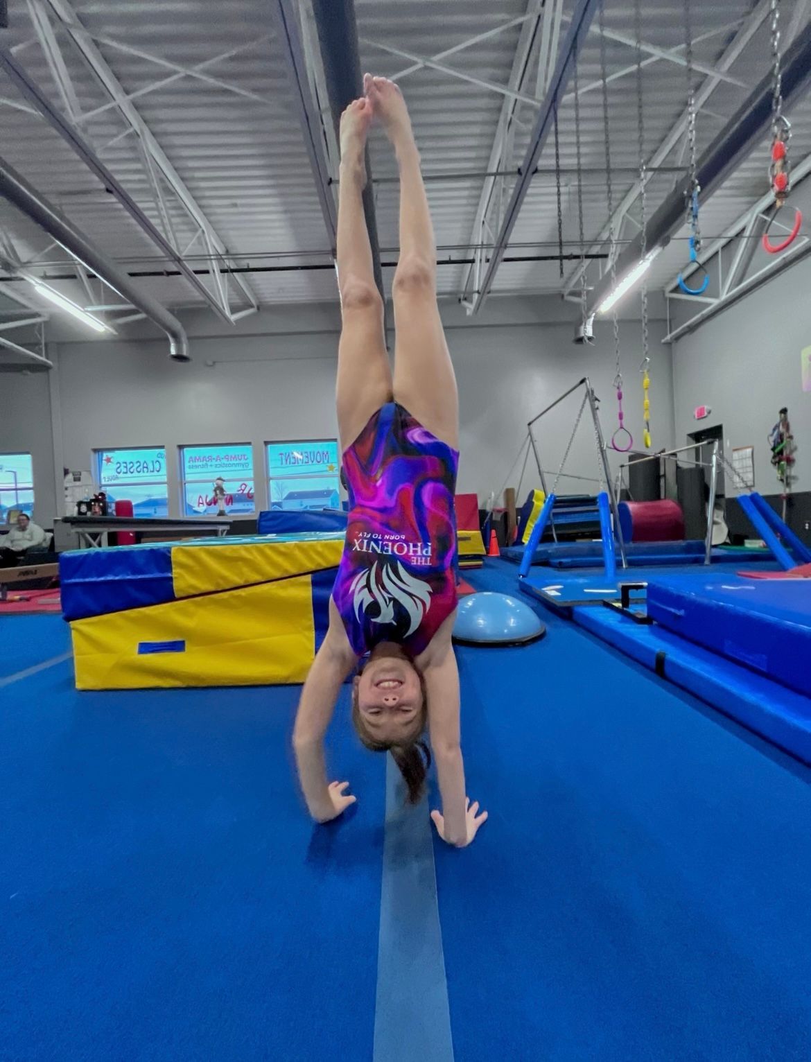 A young girl is doing a handstand on a balance beam in a gym.