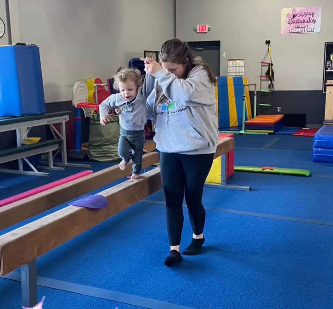 A woman and child are walking on a balance beam in a gym