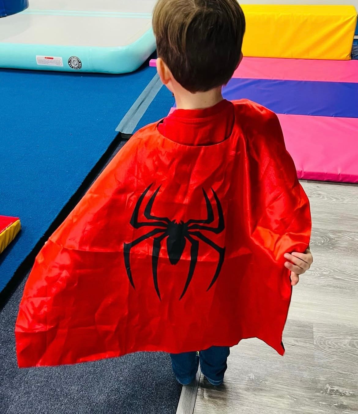 A young boy is wearing a red cape with a spider on it.
