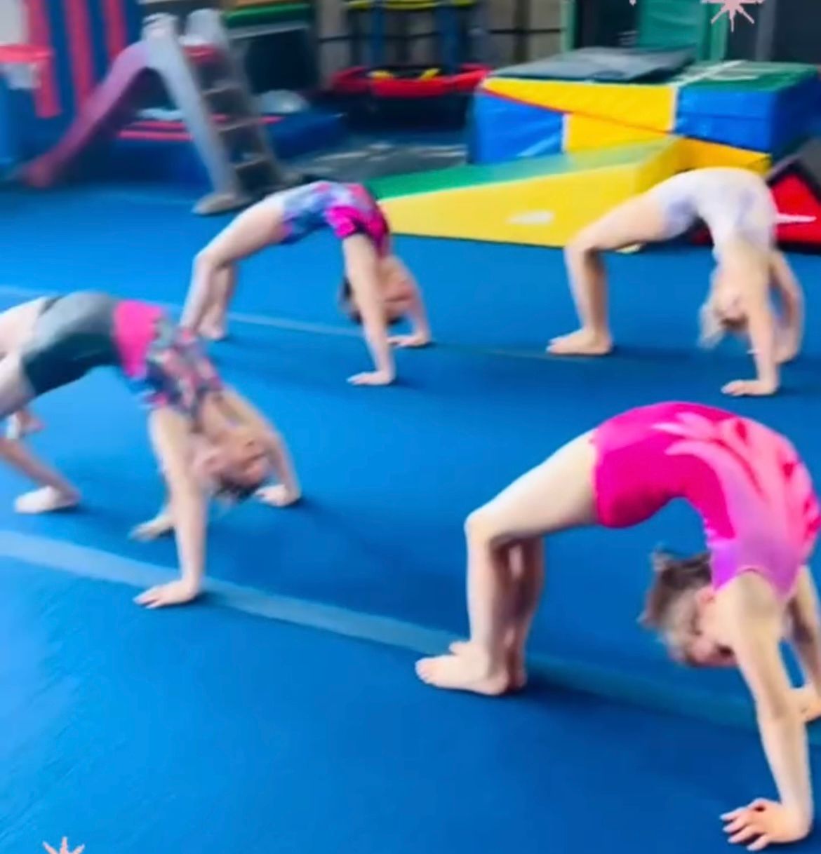 A group of young children are jumping on a balance beam in a gym.