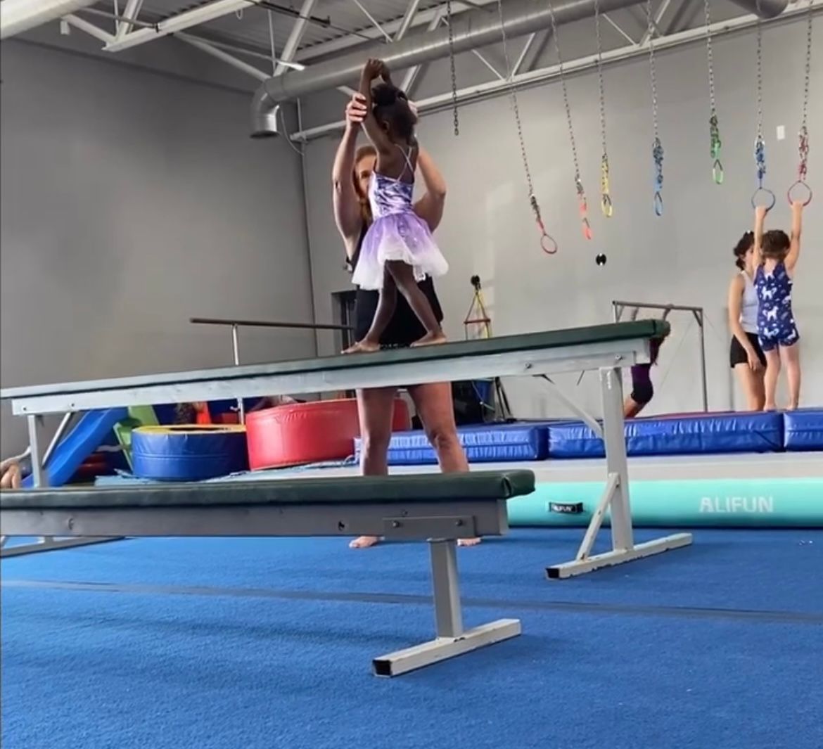 A little girl is standing on a balance beam in a gym