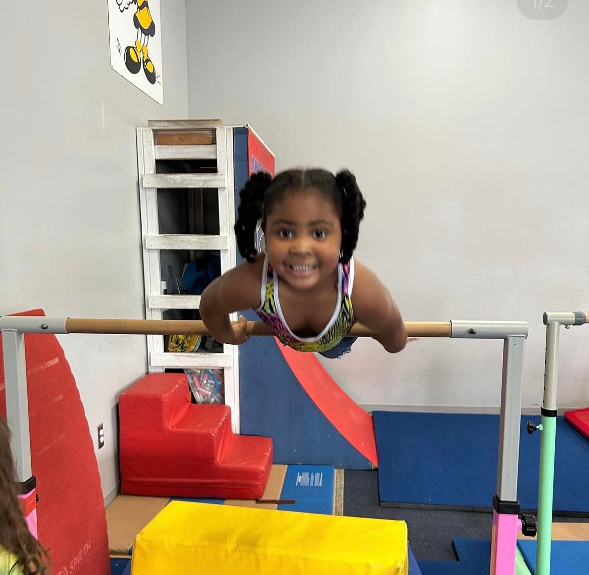 A little girl is doing a handstand on a bar in a gym.