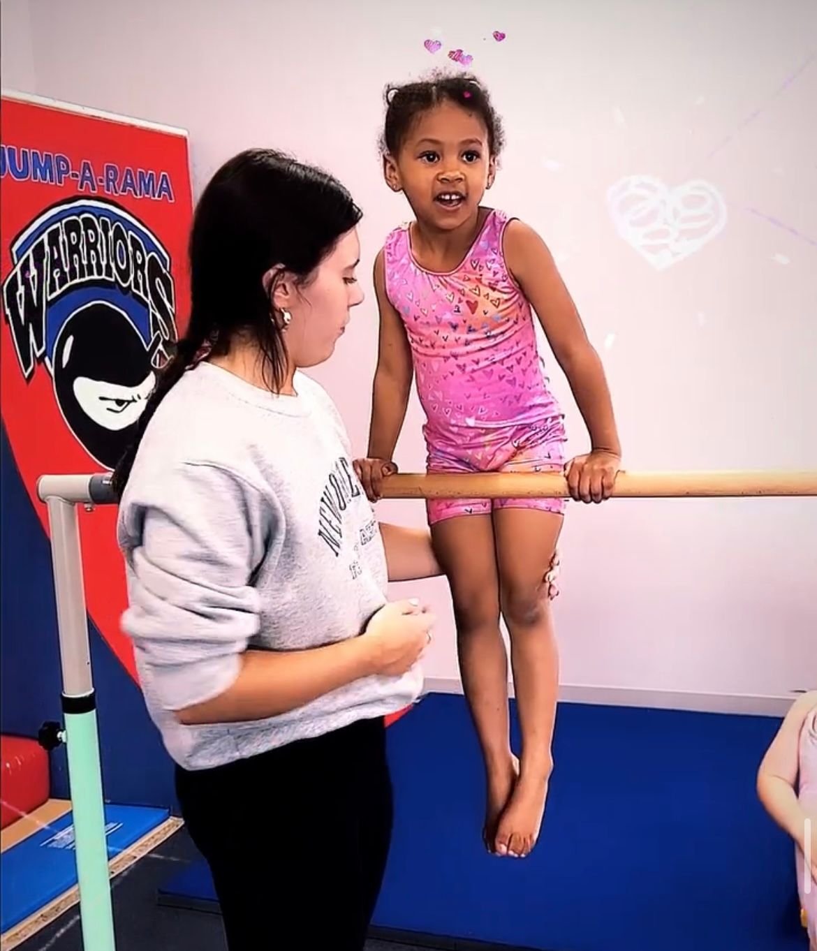 A little girl is sitting on a bar in front of a sign that says warriors