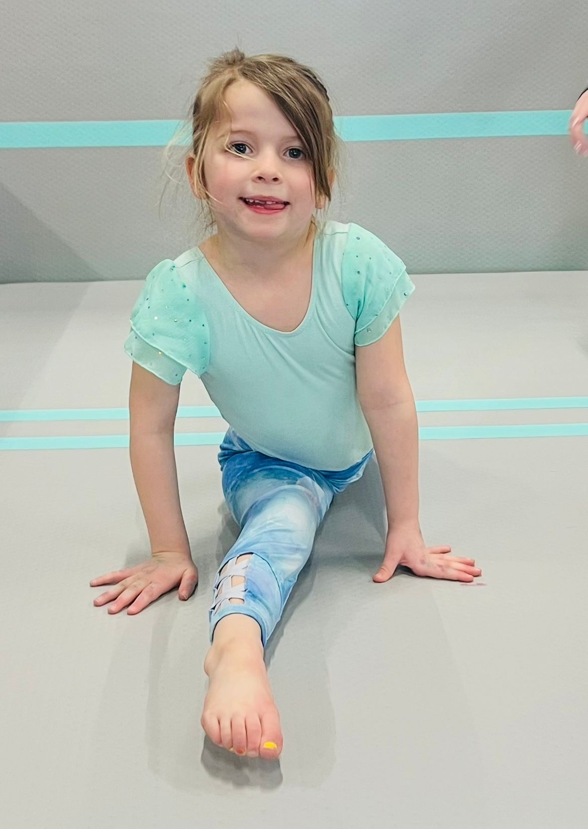 A little girl is sitting on the floor doing a split.