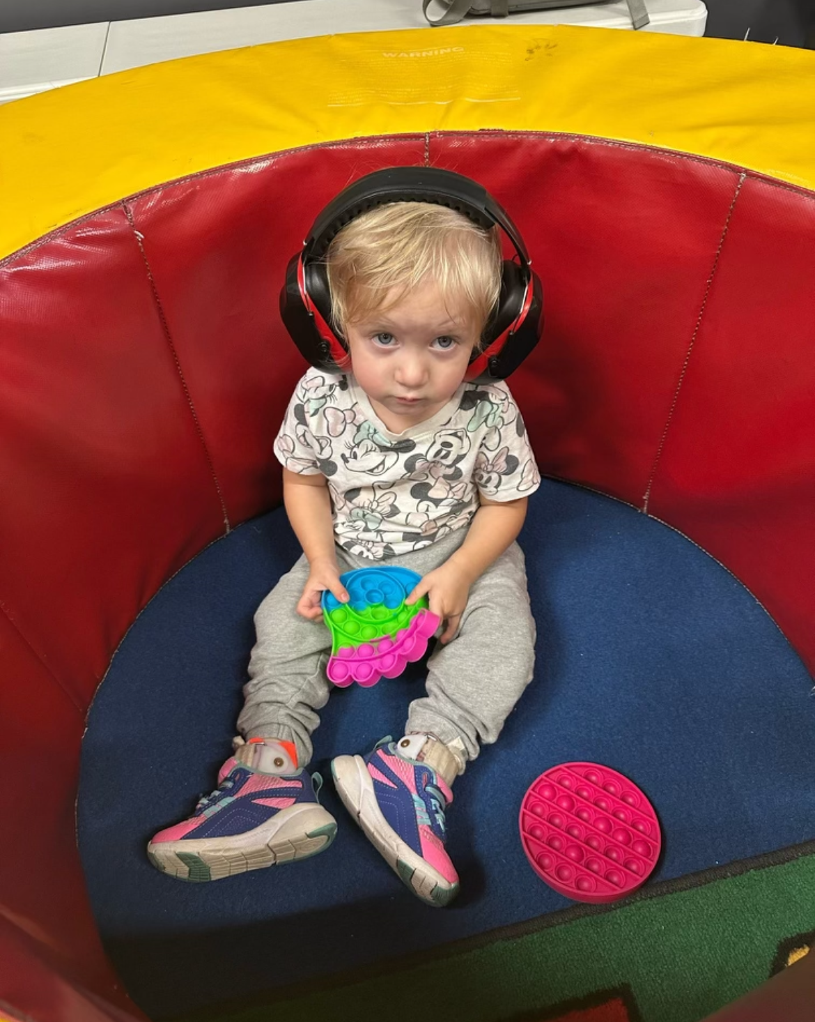 A little boy wearing headphones is sitting in a ball pit holding a toy.