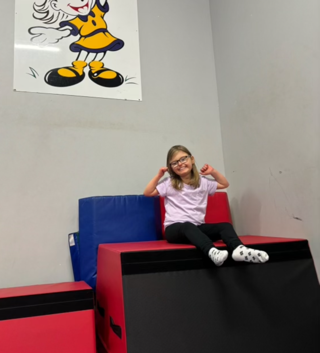 A little girl is sitting on a bench with a cartoon character on the wall behind her