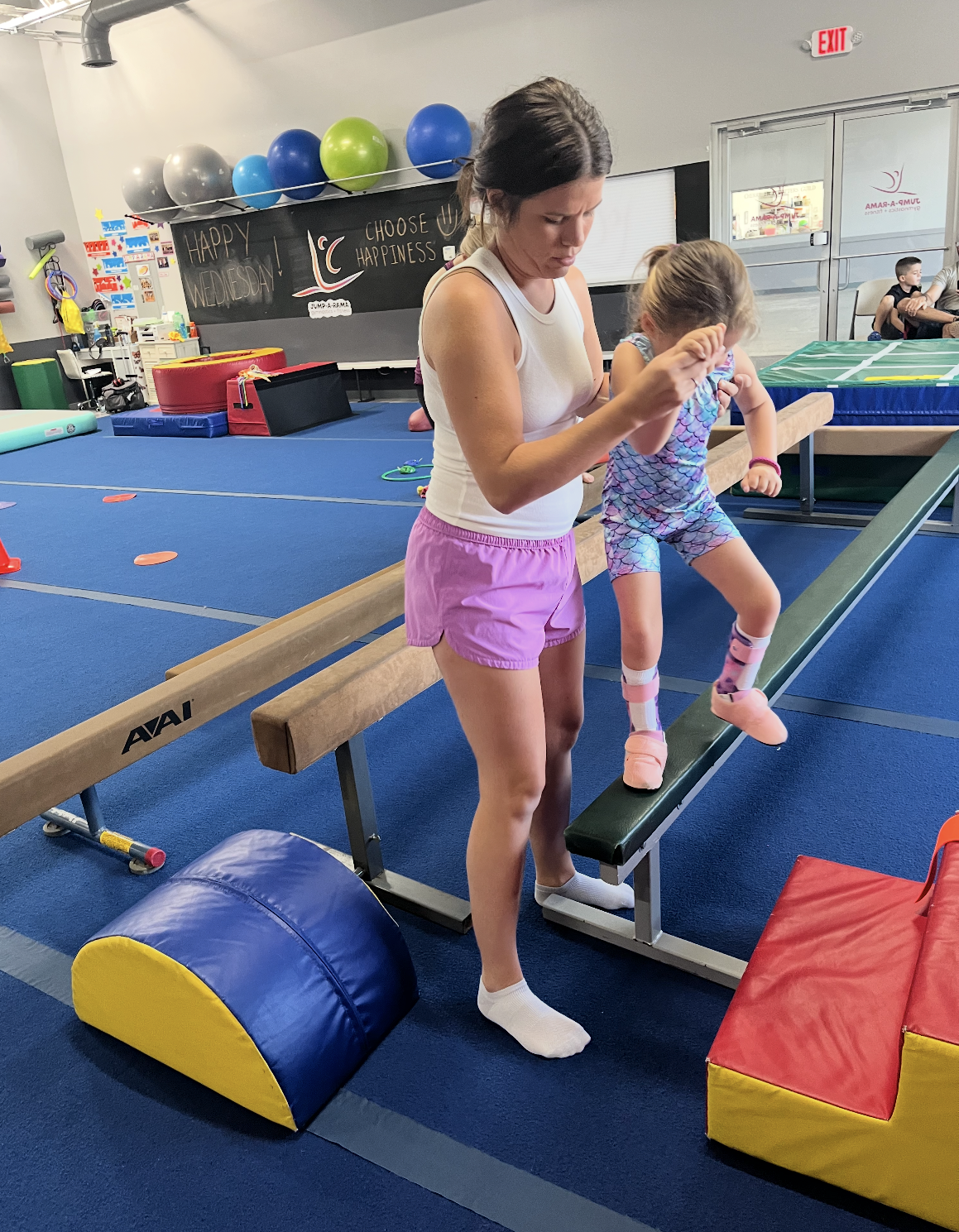 A woman is helping a little girl balance on a balance beam